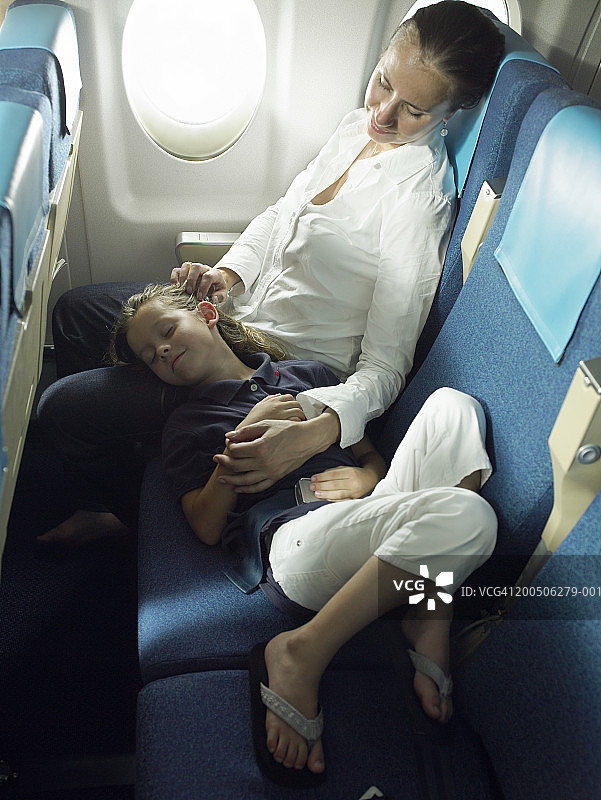 女儿(5-7岁)在飞机上睡在母亲的膝盖上图片素材