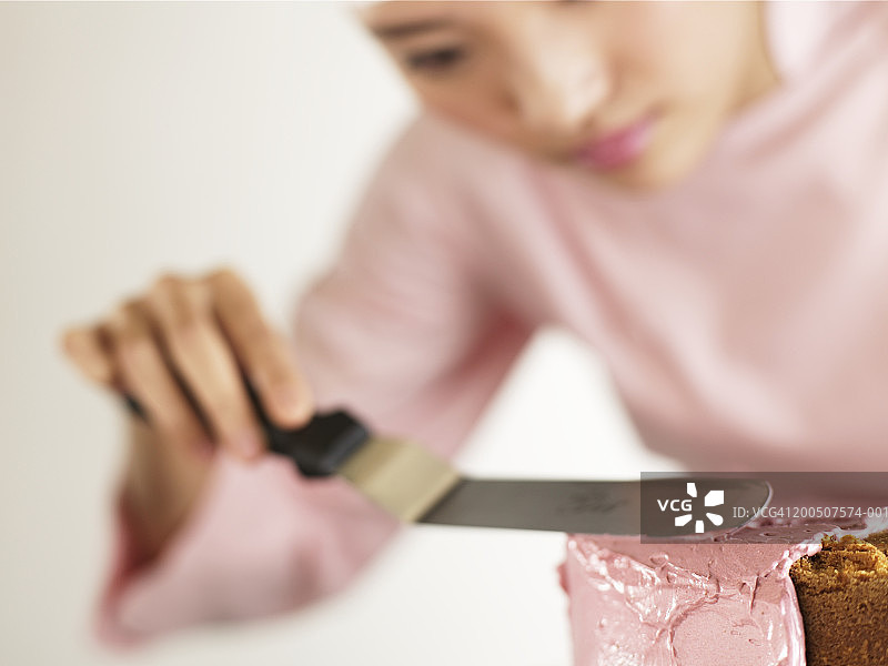 年轻女子用刮刀给蛋糕抹糖霜（柔焦）图片素材