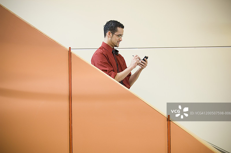 在台阶上使用掌上电脑的年轻男人，侧视图图片素材
