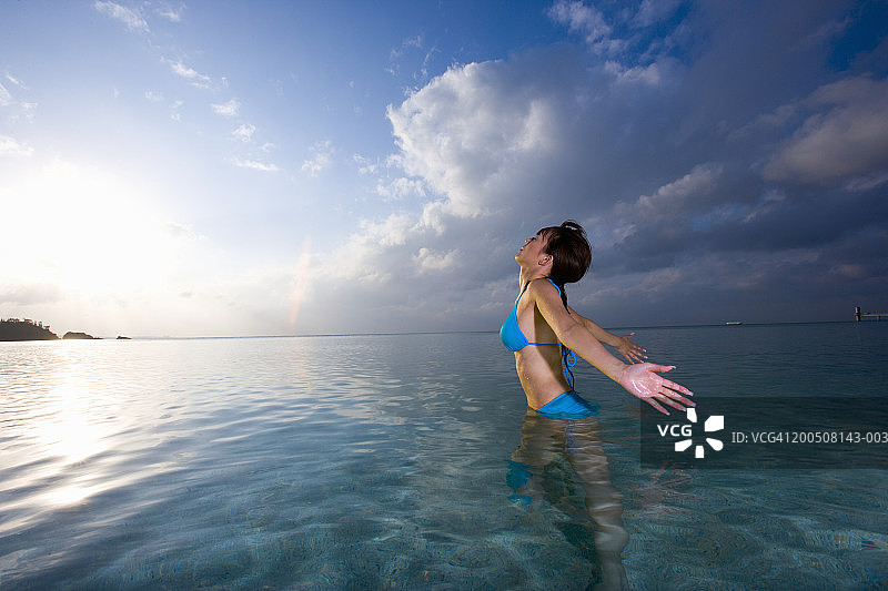 年轻女子在海中跋涉，张开双臂，头向后仰，侧视图图片素材
