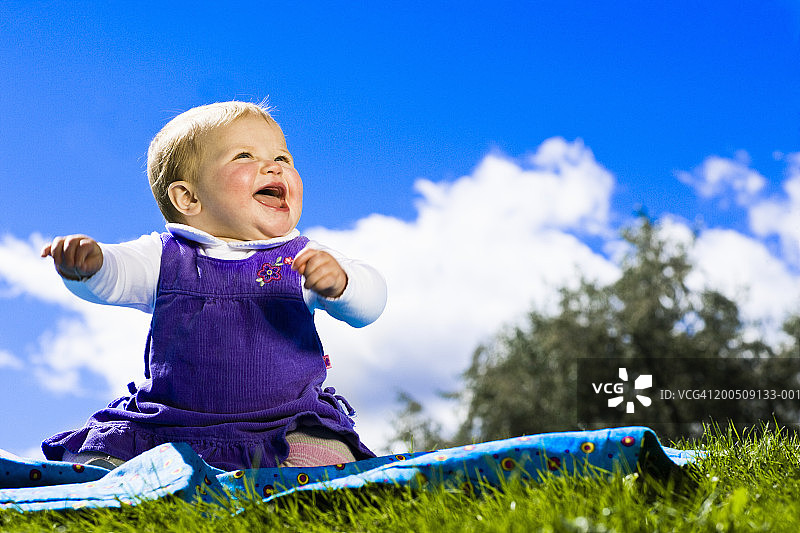 坐在草地上微笑的婴儿女孩，地面视角图片素材