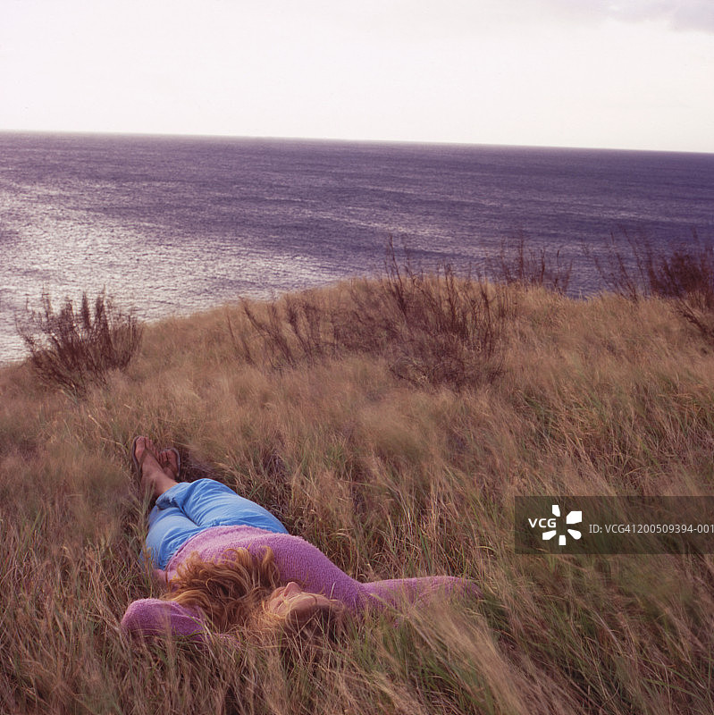 女人躺在海边高高的草丛中，日落时分（长曝光）图片素材
