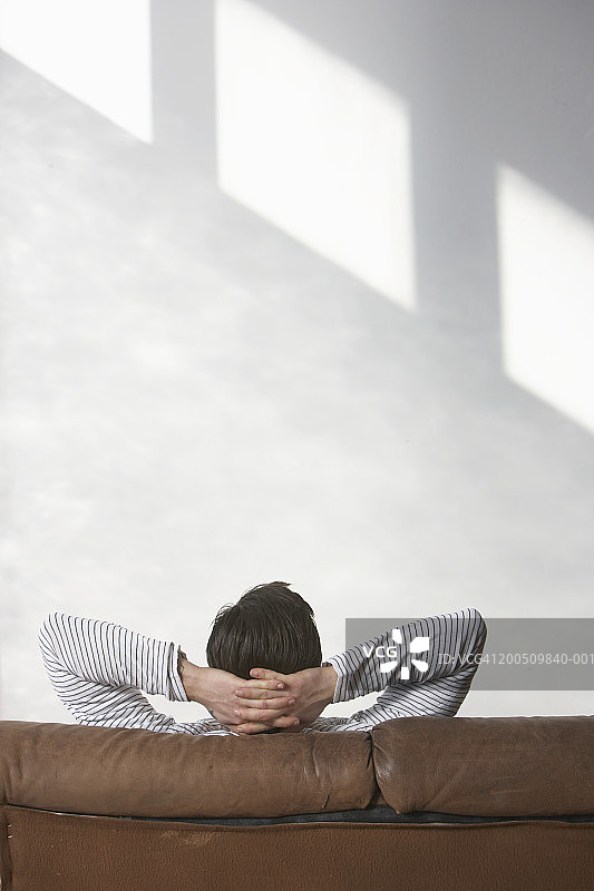 男子坐在沙发上，双手放在脑后，后视图图片素材