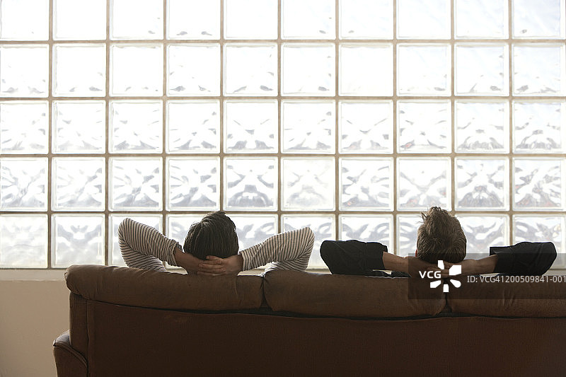 男士坐在沙发上，双手放在脑后，后视图图片素材
