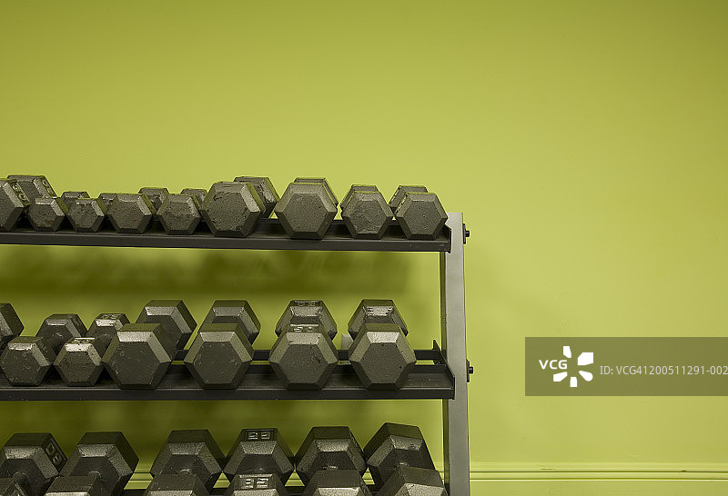 绿色墙壁旁机架上排列的精选哑铃图片素材