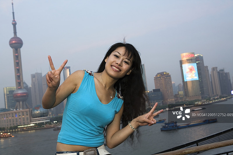 中国上海浦东：年轻女子在天际线下微笑并做出V字手势图片素材