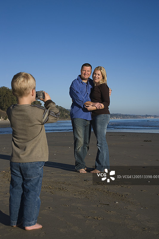 日落时分，男孩(2-4岁)在海滩上给父母拍照图片素材