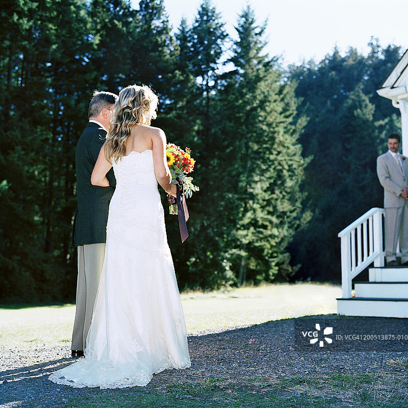 新娘和父亲站在教堂外，新郎站在背景中图片素材