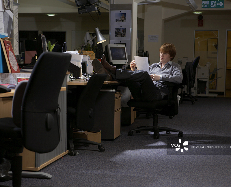 在空荡荡的办公室里把脚放在桌子上的年轻男人图片素材