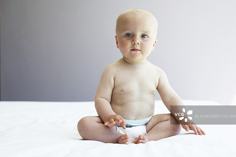 坐在床上穿着尿布的男婴（9-11个月大）肖像图片素材