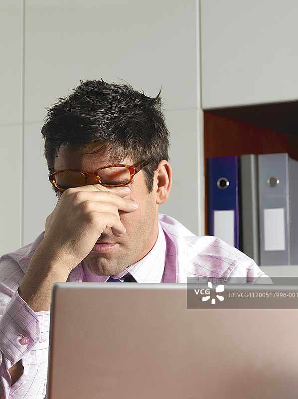 在办公室揉眼睛的笔记本电脑前的商人图片素材