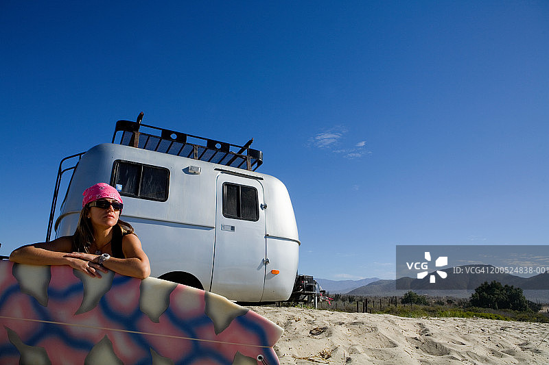 在海滩上拿着冲浪板的女人，背景是房车图片素材