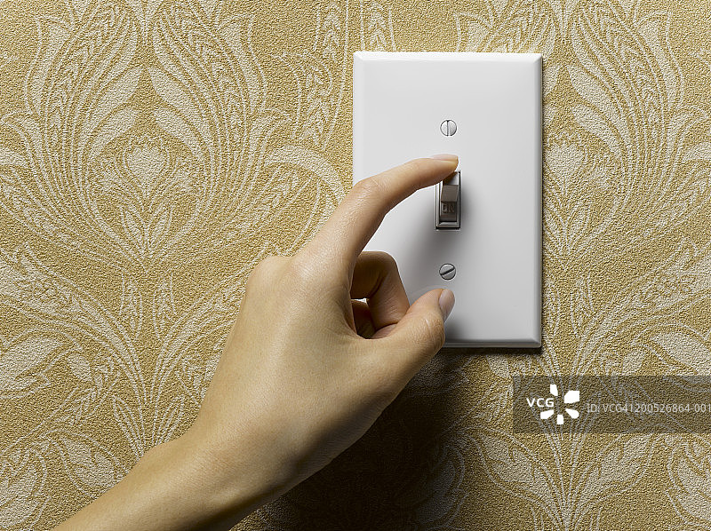 特写：女人关掉米色壁纸墙上的电灯开关图片素材