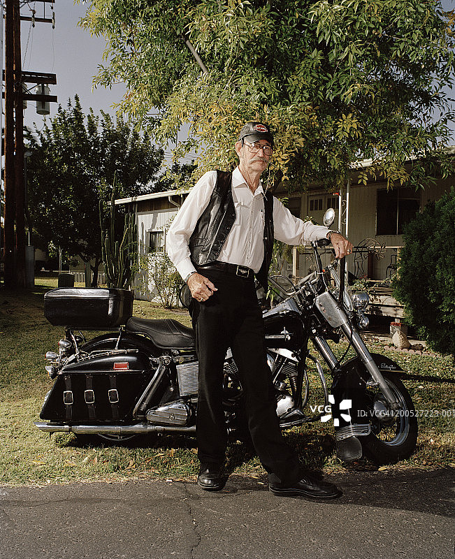 老年男人靠在摩托车上在房前院子里图片素材