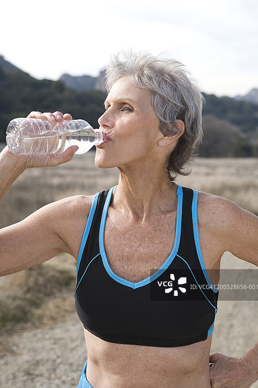 年长的女人穿着运动服在泥泞的跑道上喝水图片素材