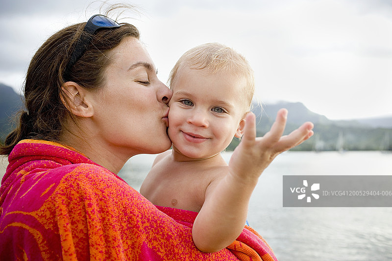 母亲在海滩上亲吻幼儿儿子的脸颊图片素材