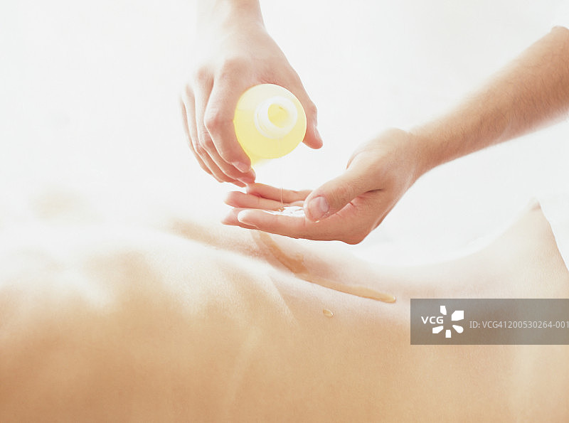 按摩师准备为男人背部涂抹精油。图片素材