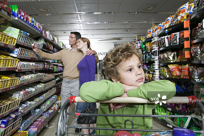 男孩（6-8岁）在超市里靠在购物车上图片素材