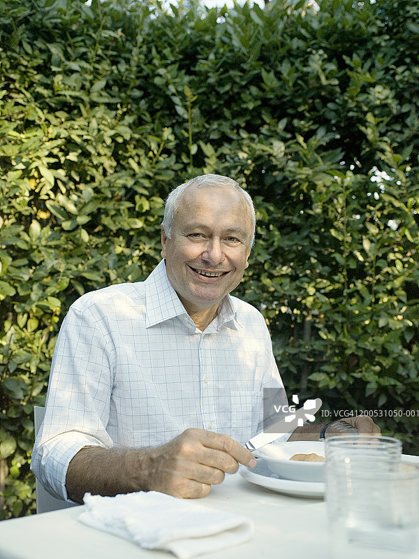 中年男人在花园餐桌旁吃东西，微笑肖像图片素材