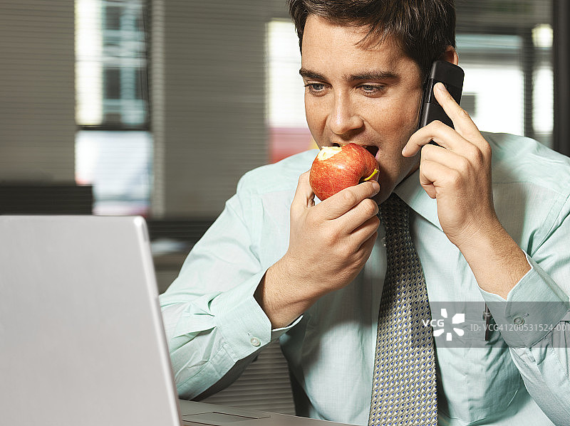 商人使用手机吃苹果看笔记本电脑图片素材
