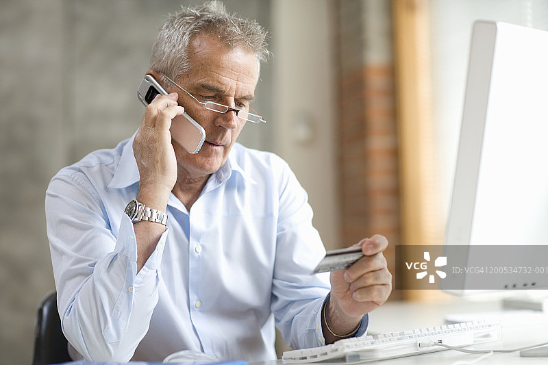 商人坐在电脑前使用手机，看着银行卡图片素材