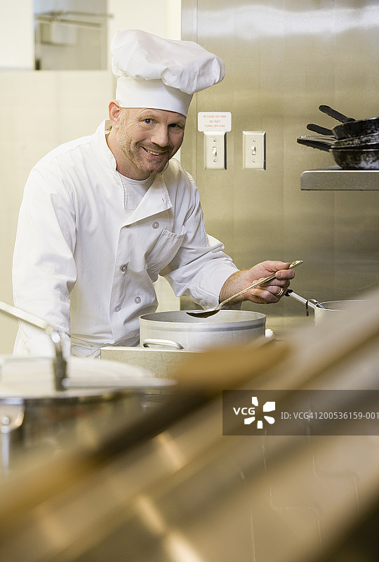 手持勺子站在炉灶前、对着锅的成熟男厨师图片素材