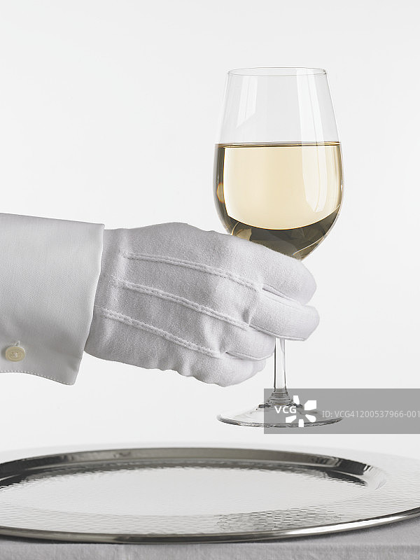 戴手套的服务员端着一杯白葡萄酒图片素材