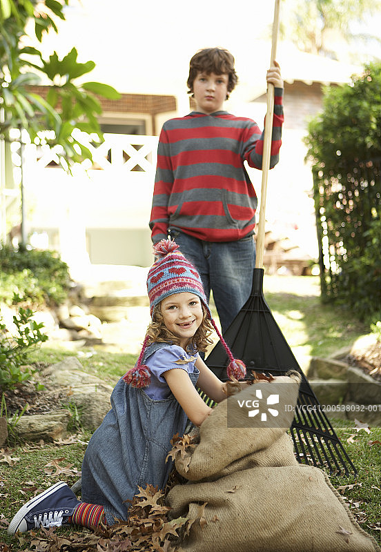 男孩和女孩(6-10岁)在花园里耙树叶，微笑肖像图片素材