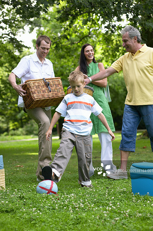 在公园里和家人一起踢球的男孩（6-8岁），带着野餐物品图片素材