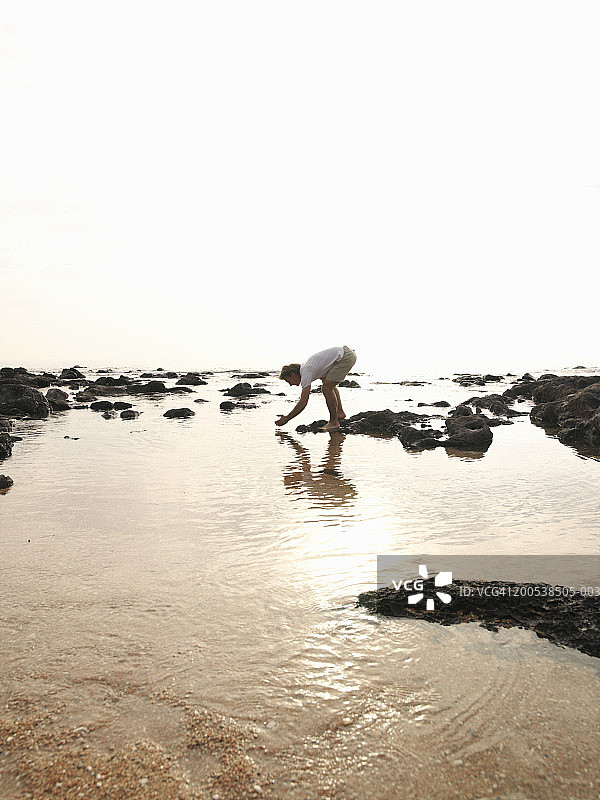 意大利撒丁岛戈诺内海湾，男人从潮汐池中舀水图片素材