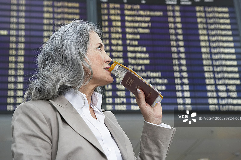 拿着护照站在航班信息显示屏旁的中年女商人图片素材