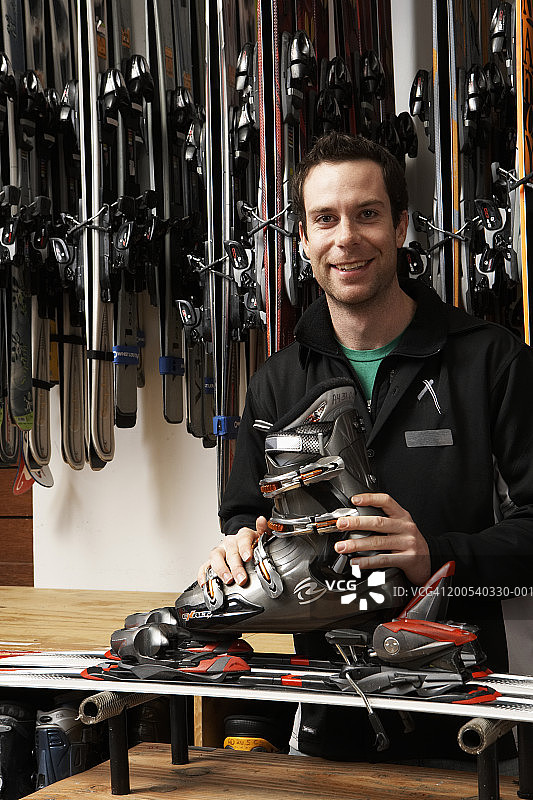 年轻男人在体育用品店检查滑雪靴、滑雪板和固定器，肖像照图片素材