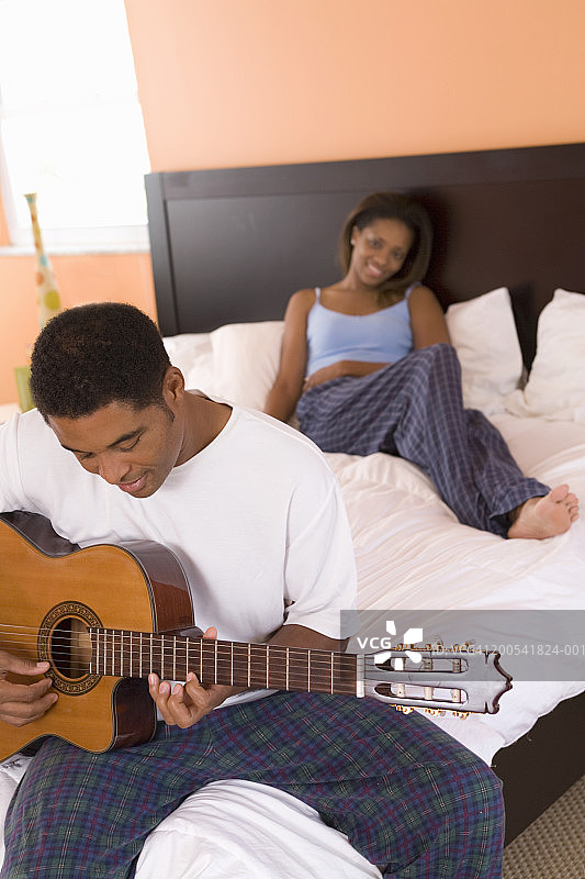 中年男人和年轻女人坐在床上，男人弹着原声吉他图片素材