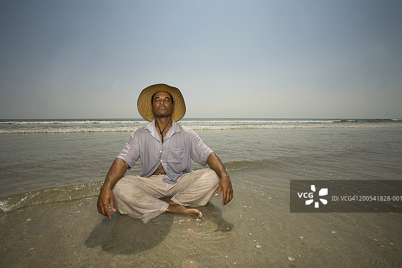 戴着遮阳帽坐在海浪中，闭着眼睛的中年男人图片素材
