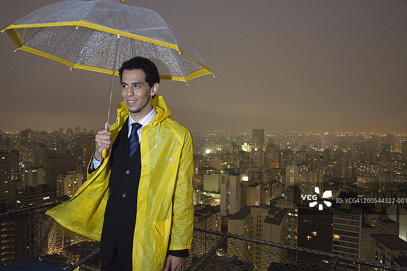 在城市景观前，身穿雨衣、带雨伞的商人图片素材