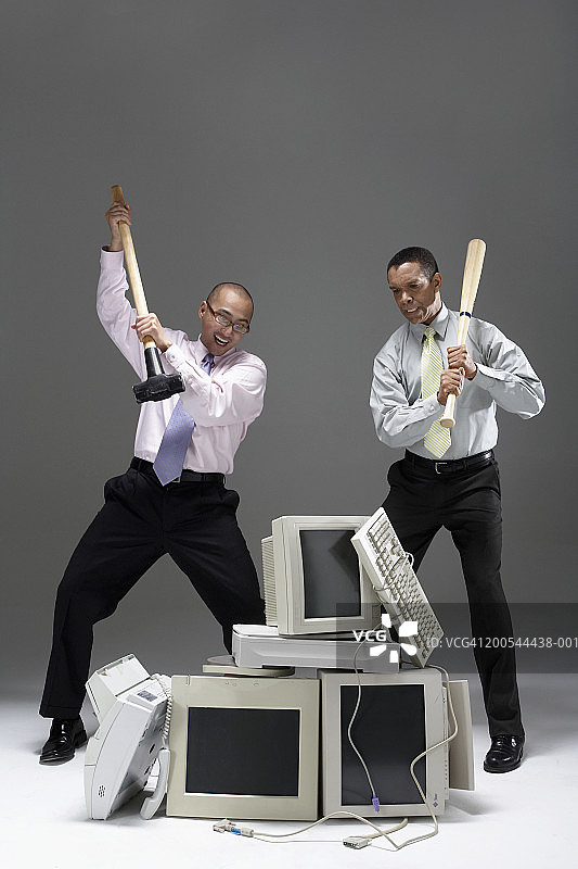 两位商人拿着大锤和棒球棒，靠近一堆旧技术设备图片素材