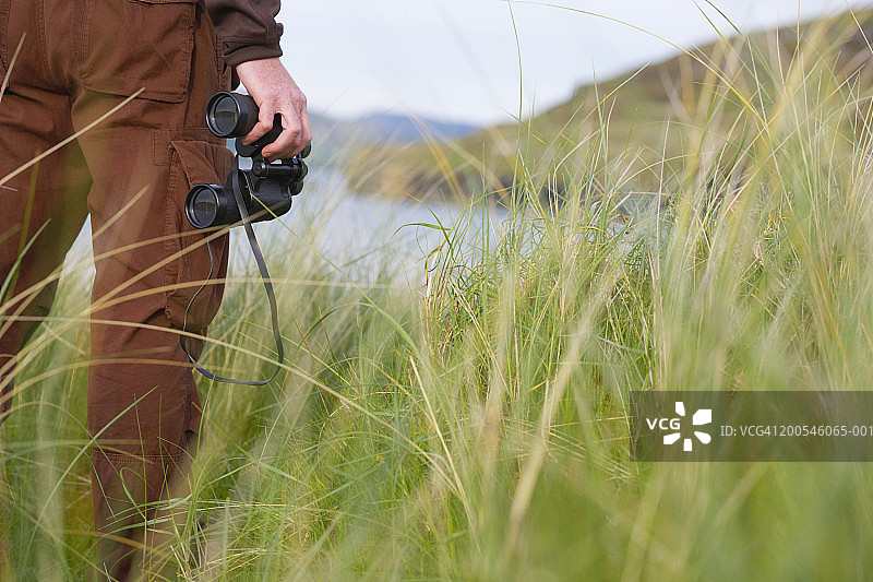 爱尔兰阿尔斯特多尼戈尔巴利马斯托克海湾，拿着双筒望远镜的男人图片素材