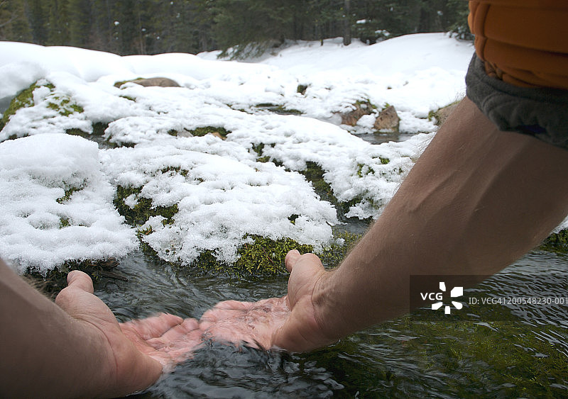 男人从雪山溪流中舀水（特写）图片素材