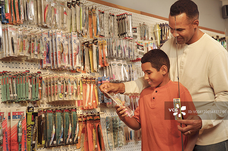 父亲和儿子(12-13岁)在商店购买渔具，面带微笑图片素材