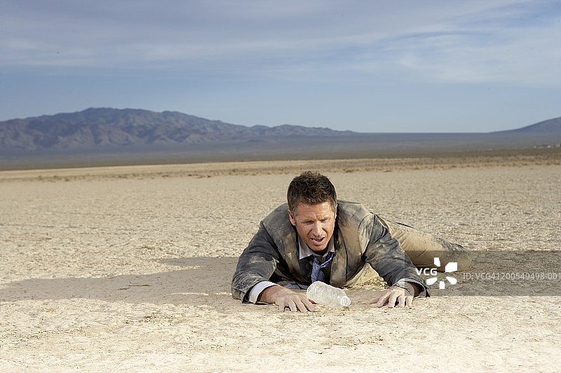 商务男士在干涸的湖床上挣扎，看着空水瓶图片素材