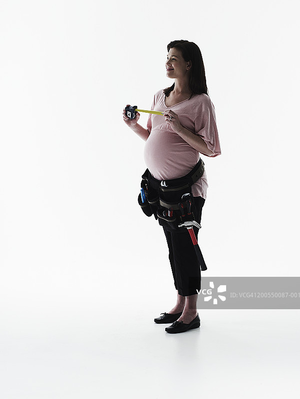 戴工具腰带、拿卷尺的孕妇图片素材