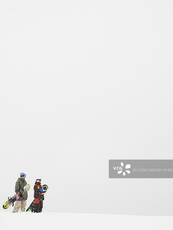 年轻男女带着滑雪板在山顶，侧面视角图片素材