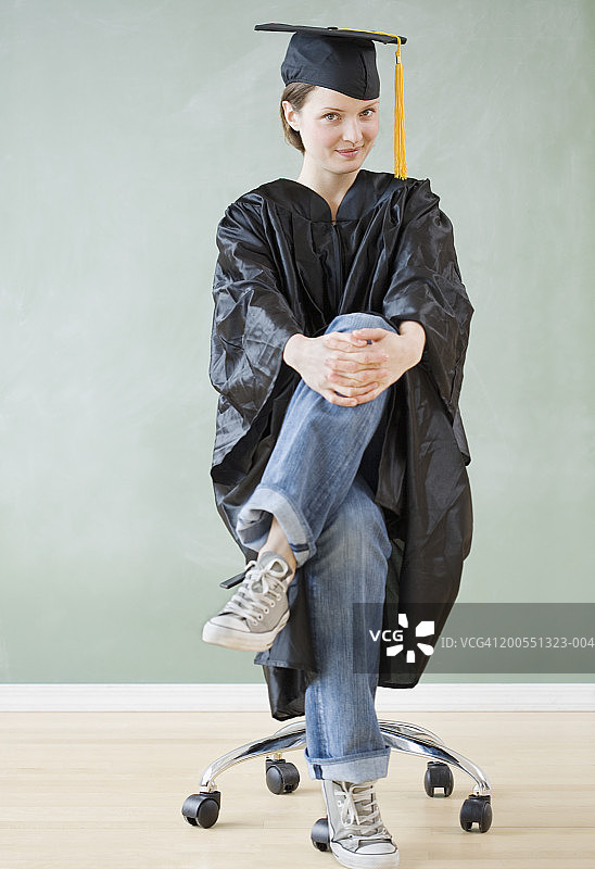 穿着毕业礼服坐在凳子上微笑的年轻女人肖像图片素材