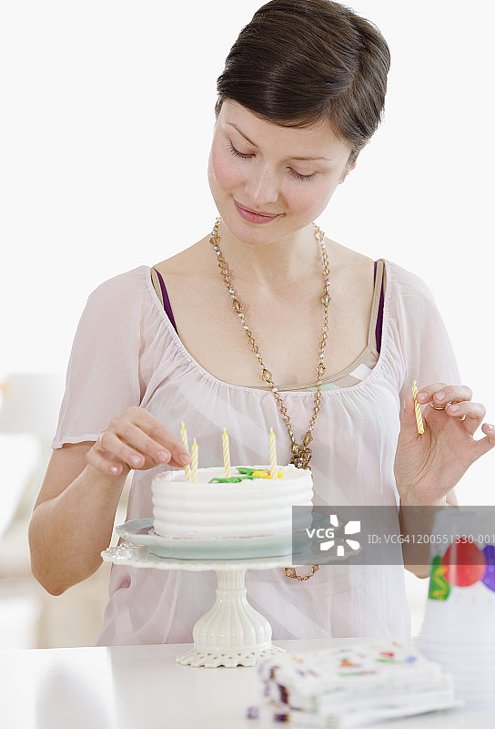 年轻女子在生日蛋糕上插蜡烛，面带微笑图片素材