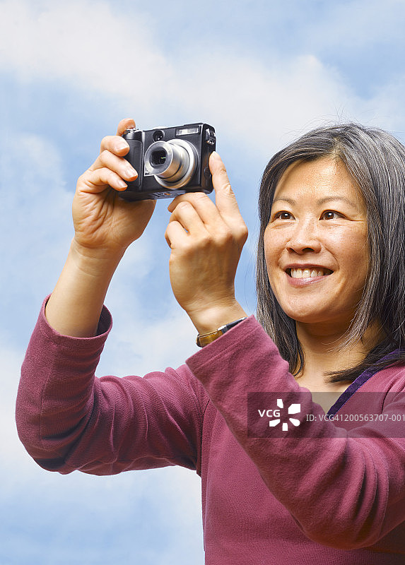 对着天空，使用数码相机微笑的中年妇女图片素材