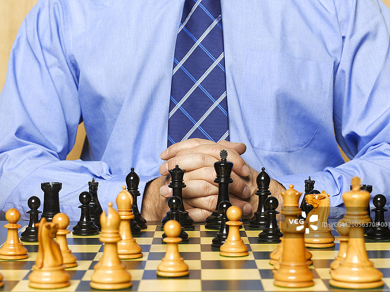 男人坐在棋盘前双手紧握，中段视角图片素材