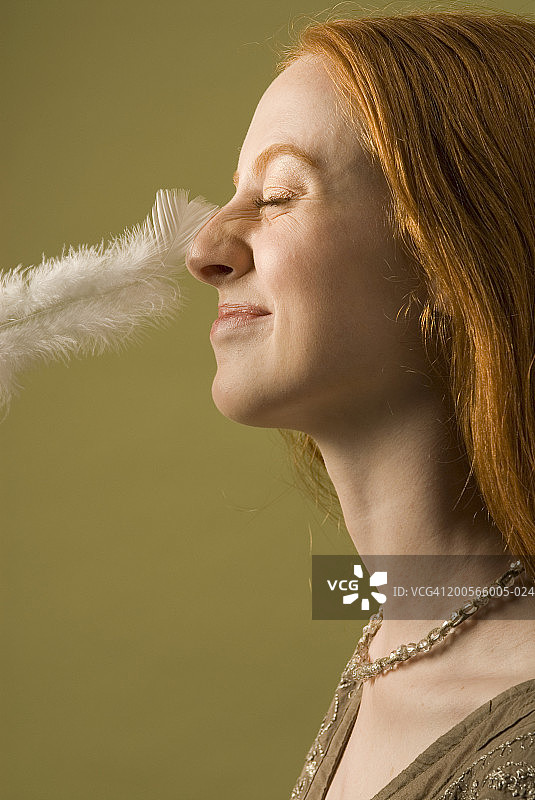 羽毛轻触鼻子，年轻女人的侧脸图片素材