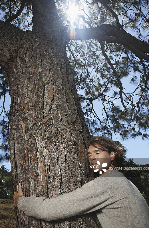 闭着眼睛拥抱树的年轻男人图片素材