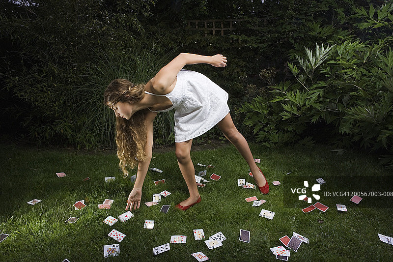 草地上，10-11岁的女孩捡起一张方块A图片素材