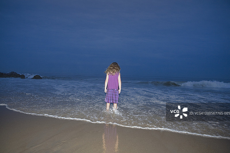 小女孩站在海滩的浅水中，后视图，夜晚图片素材